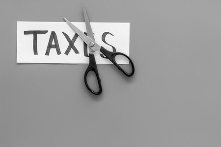 Cut taxes concept. Scissors cut paper with word Taxes on grey background top view space for textの写真素材