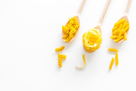 Various types of pasta concept. Fusilli, penne, fettuccine in spoons on white background top view copy spaceの写真素材