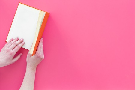 Open the book. Hands hold hardback book opened on pink background top view copy spaceの写真素材