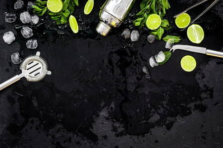 Ingredients and crockery for making mojito. Slices of lime, mint, sugar cubes, glass with ice cubes, shaker, strainer on black background top view.の写真素材