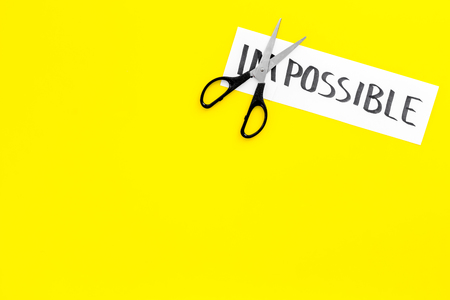 Belief in yourself concept. Cutting the part im of written word impossible by scissors. Yellow background top view.の写真素材