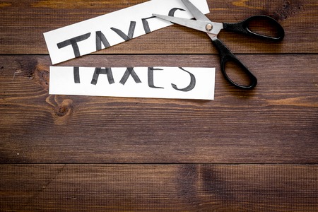 Cut taxes concept. Scissors cut paper with word Taxes on dark wooden background top view.の写真素材