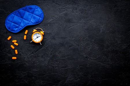 Medicine helps get asleep. Good sleep. Sleeping pills near sleeping mask and alarm clock on black background top view copy spaceの写真素材