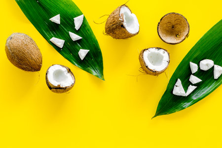 Coconut background. Whole and cut coconuts, pulp and palm leaves on yellow background top view copy...