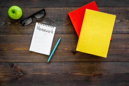 Homework concept. Word homework written in notebook on dark wooden desk with textbooks, tutorials and apple top view copy spaceの写真素材