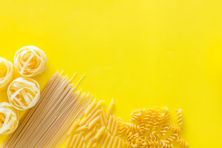 Types of pasta. Raw spaghetti, fusilli, penne, fettuccine on yellow background top view.の写真素材