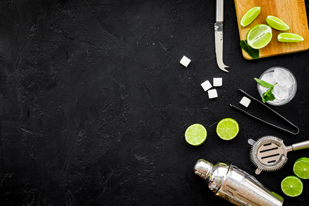 Make mojito cocktail with lime and mint. Shaker, strainer, glass near slices of lime on cutting board on black background top view.の写真素材