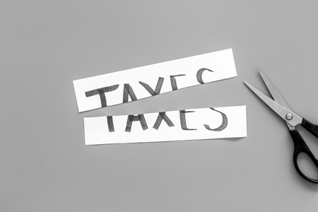 Cut taxes concept. Sciccors cut paper with word Taxes on grey background top view.の写真素材
