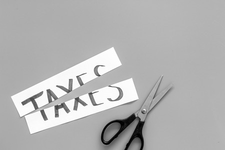 Cut taxes concept. Scissors cut paper with word Taxes on grey background top view.の写真素材