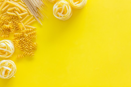 Set of pasta. Raw spaghetti, fusilli, penne, fettuccine on yellow background top view.の写真素材