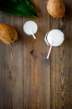 Tropical alcohol-free beverage. Fresh coconut milk in glasses with straw near coconut and palm leaves on dark wooden background top view.の写真素材