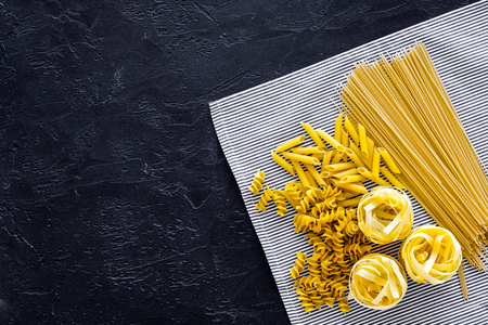 Assortment of raw pasta. Spaghetti, fusilli, penne, fettuccine on blue tablecloth on black background top view.の写真素材