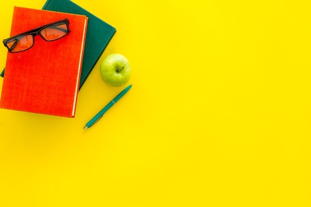 Educational literature. School textbook, book, tutorial, apple and glasses on yellow background top view copy spaceの写真素材