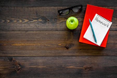 Homework concept. Word homework written in notebook on dark wooden desk with textbooks, tutorials and apple top view copy spaceの写真素材