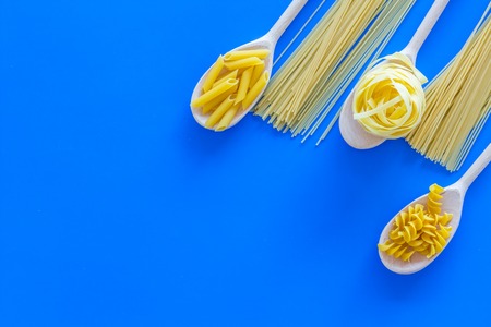 Various pasta concept. Fusilli, penne, fettuccine in spoons on blue background top view.の写真素材