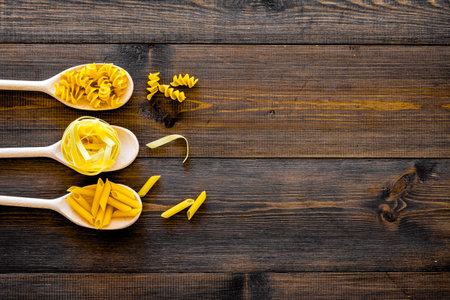 Various pasta concept. Fusilli, penne, fettuccine in spoons on dark wooden background top view.の写真素材