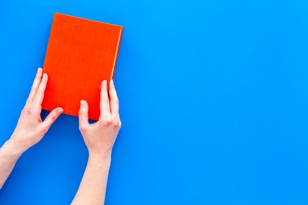 Reading for leisure. Hands take hardback book with empty cover on blue background top view.の写真素材