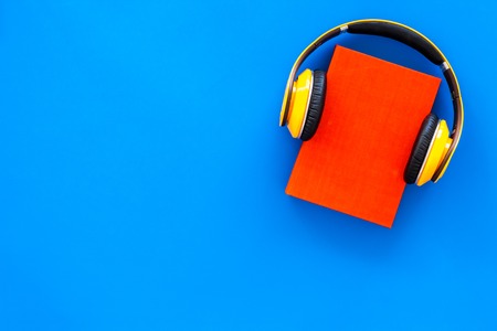 Audiobooks concept. Headphones put over hardback book with empty cover on blue background top view.の写真素材