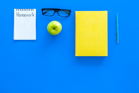 Homework concept. Word homework written in notebook on blue desk with textbooks, tutorials and apple top view.の写真素材