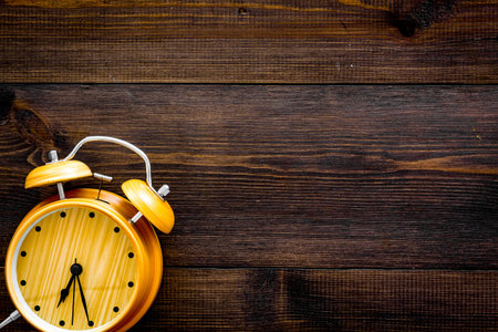 Alarm clock for for waking up on dark wooden background top view copy space