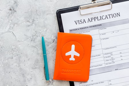 Visa prosessing. Registration of visas. Visa application form, pen, passport cover with airplane silhouette on grey background top view copy spaceの写真素材