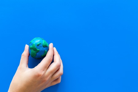 Earth. Hand hold plastiline symbol of planet Earth globe on blue background top view.の写真素材