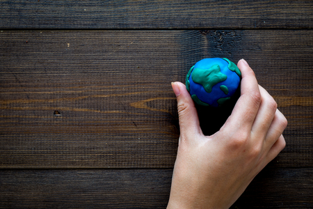 Earth. Hand hold plastiline symbol of planet Earth globe on dark wooden background top view.の写真素材