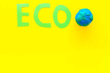 Eco icon cutout near planet Earth plastiline symbol on yellow background top view.の写真素材