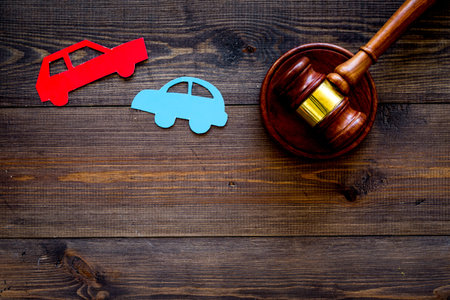 Car accident lawsuit concept. Two collided cars near judge gavel on dark wooden background top view.