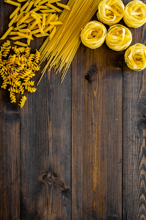 Set of pasta frame. Uncooked spaghetti, fusilli, penne, fettuccine on dark wooden background top view copy spaceの写真素材