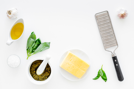Cook homemade pesto sauce. Cheese, garlic, green basil, olive oil, salt near grater and mortar on white background top view copy spaceの写真素材
