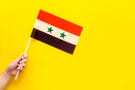 Syrian flag concept. Hand hold small flag on yellow background top view copy space