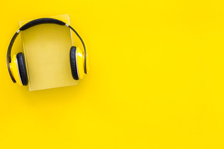 Audiobooks concept. Headphones put over hardback book with empty cover on yellow background top view.の写真素材