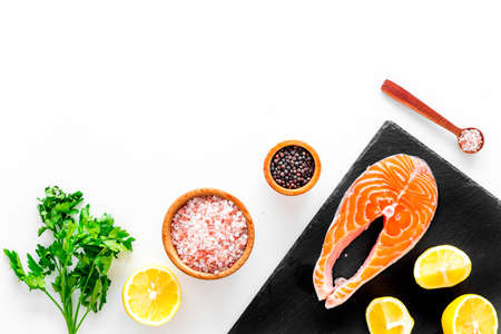 Red fish with spices. Salmon steak on cutting board near sea salt, pepper, lemon slices, greenery on white background top view space for textの写真素材