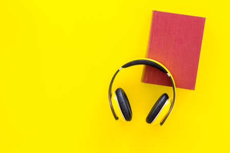 Distance education, e-learning concept. Headphones near hardback book with empty cover on yellow background top view copy spaceの写真素材