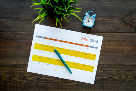 Planning concept. Goals and tasks for month. Blank month calendar near alarm clock on dark wooden...
