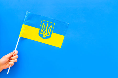 Ukrainian flag concept. Hand hold small flag on blue background top view copy spaceの写真素材