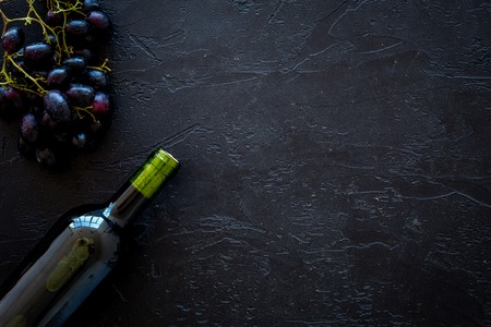 Red wine concept. Glass bottle with beverage near bunch of grapes on black background top view copy spaceの写真素材
