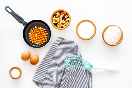 Preparing belgian waffles. Waffle on pan near whisk for whipping and ingrdients. Eggs, flour, sugar, dried fruits on white background top view.の写真素材