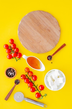 Ingredients for cooking pizza. Cherry tomatoes, olive oil, cheese mozzarella, spices on yellow background top view.の写真素材