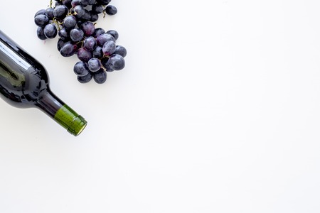 Red wine concept. Glass bottle with beverage near bunch of grapes on white background top view.の写真素材