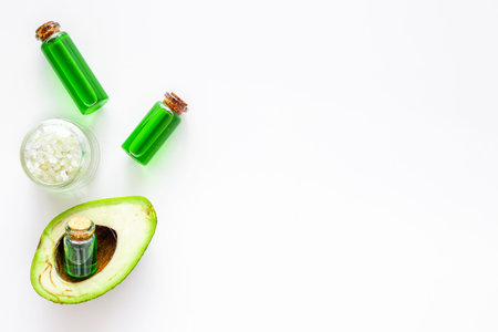 Cosmetics for skin care. Avocado oil near half of avocado on white background top view copy space