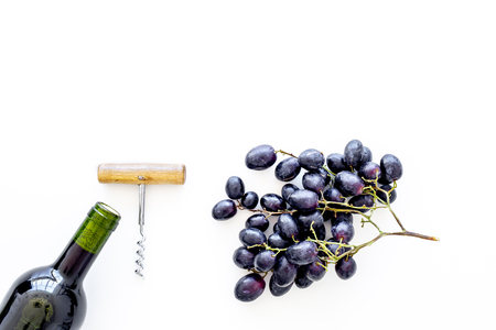 Red wine concept. Glass bottle with beverage near bunch of grapes and corkscrew on white background top view.の写真素材