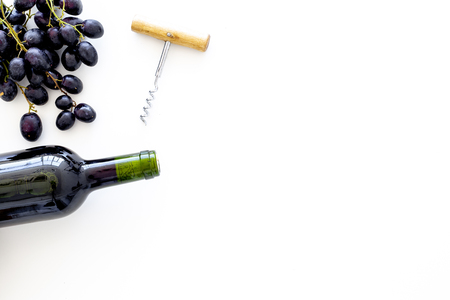 Red wine concept. Glass bottle with beverage near bunch of grapes and corkscrew on white background top view.の写真素材