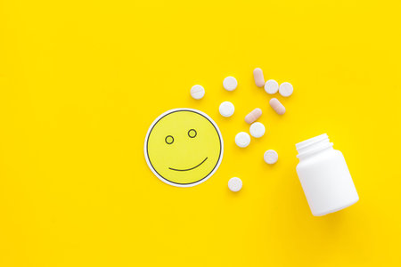 Reception of medicines concept. Recovery. Pills falling out of jar near smile face emoji on yellow background top view.の写真素材