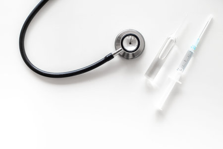 Infuenza vaccine in syringe near stethoscope on white background top view.