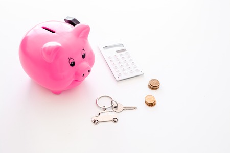 Money for buy car. Moneybox in shape of pig near keychain in shape of car, coins, calculator on white background.の写真素材
