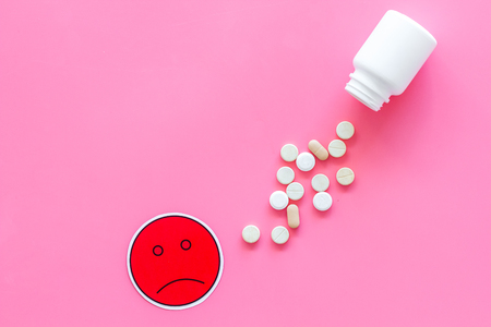 Illness. Drug intake. Pills falling out of jar near sad face emoji on pink background top view.の写真素材