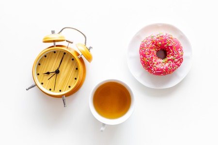 Time for breakfast concept. Tea, donut near alarm clock on white background top viewの写真素材