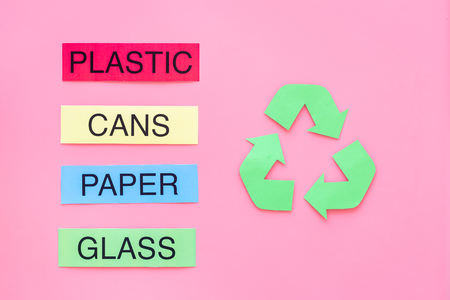 Materials suitable for recycle near green recycle eco symbol. Words paper, glass, plastic, cans on pink background top view.の写真素材